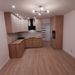 VITALII DERDIIENKO VIDE-REM - Jasna kuchnia z drewnianymi akcentami, czarnym okapem i nowoczesnym oświetleniem. Podłoga z paneli imitujących drewno. Minimalistyczny design.