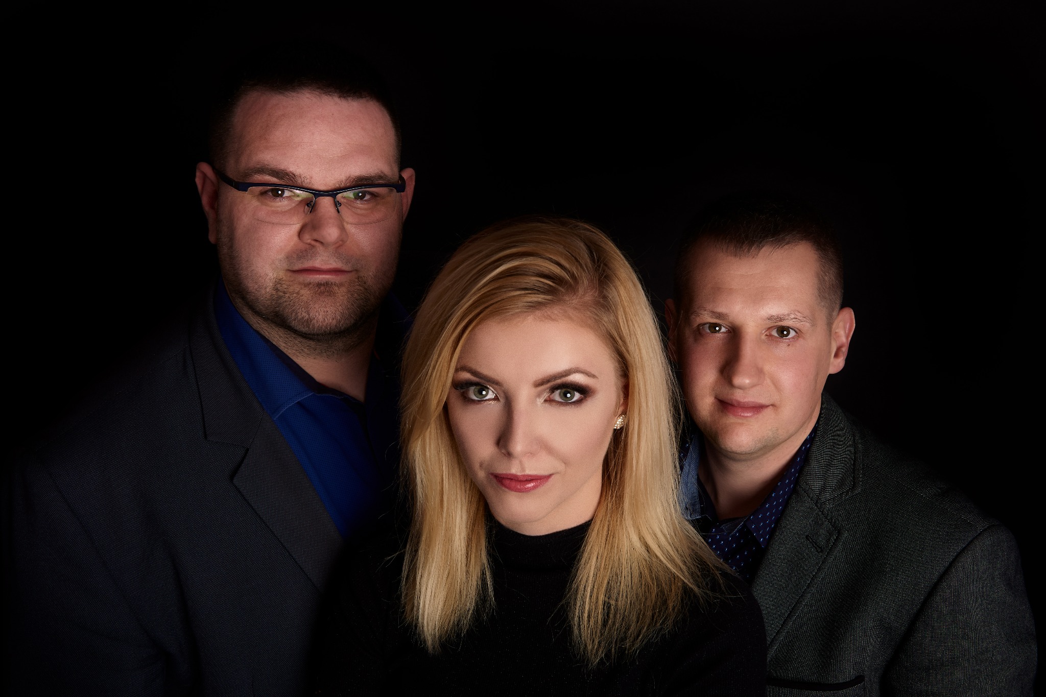 Portret studyjny: blondwłosa wokalistka w czarnym golfie z dwoma mężczyznami w garniturach na czarnym tle.