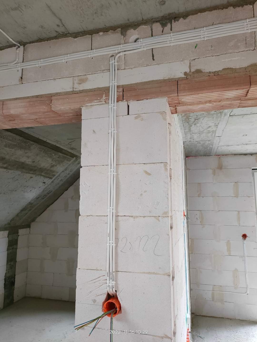 Wewnętrzna instalacja elektryczna w trakcie montażu w surowym budynku z pustaków, widoczne kable w peszlach prowadzone po ścianach i suficie, puszka instalacyjna z wystającymi przewodami.