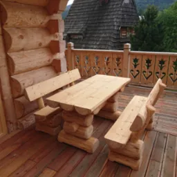 Drewniany st&oacute;ł z ławkami na tarasie z widokiem na g&oacute;rski krajobraz i tradycyjny dom z ciemną dach&oacute;wką.