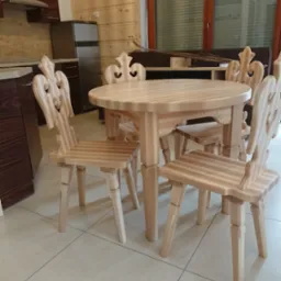 Drewniany stół z czterema krzesłami o zdobionych oparciach w stylu góralskim, widoczne w kuchni z drewnianą boazerią.