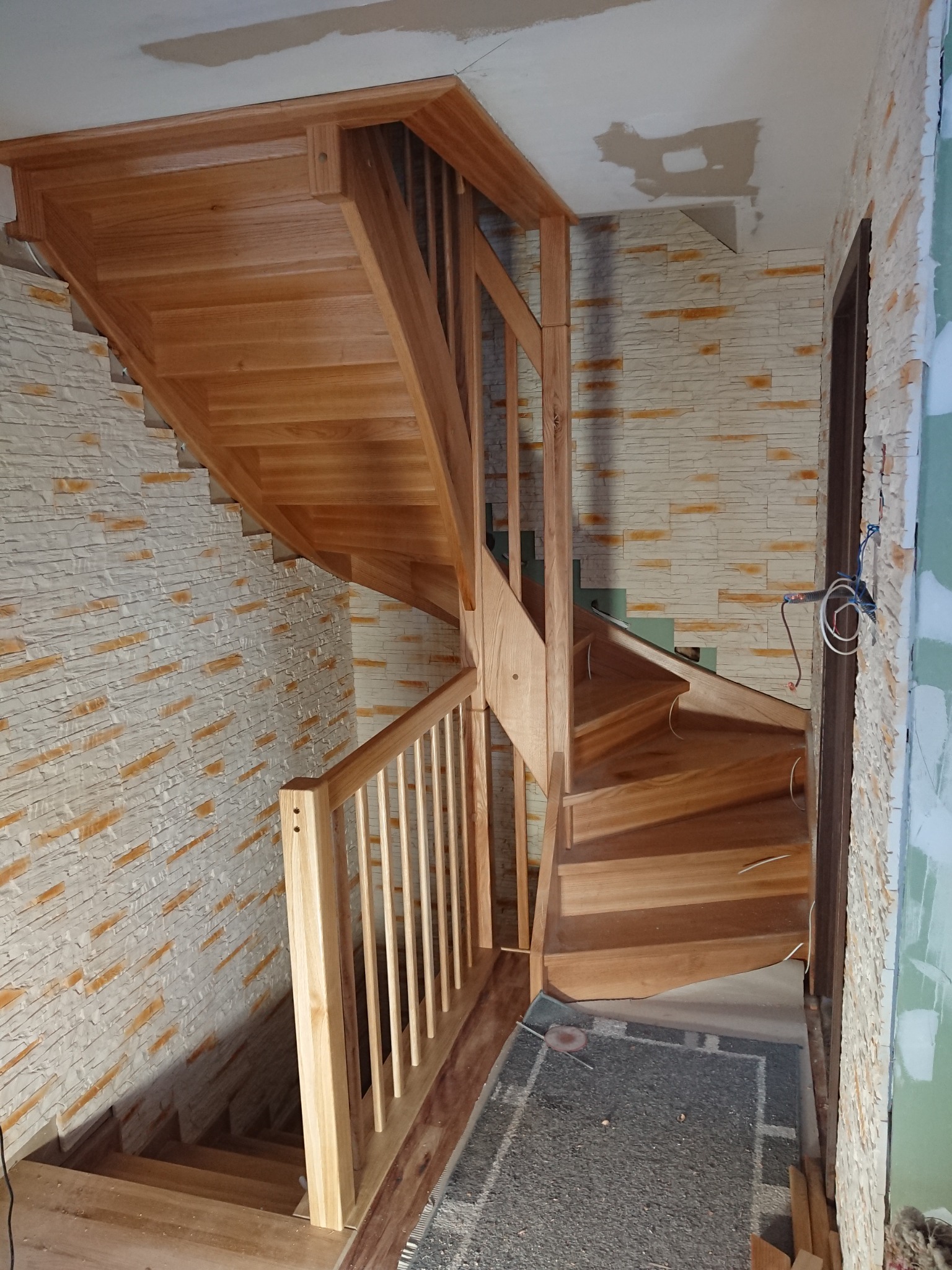 Drewniane schody kręcone z balustradą, widoczne w trakcie montażu, z fragmentami niedokończonych ścian i sufitu.