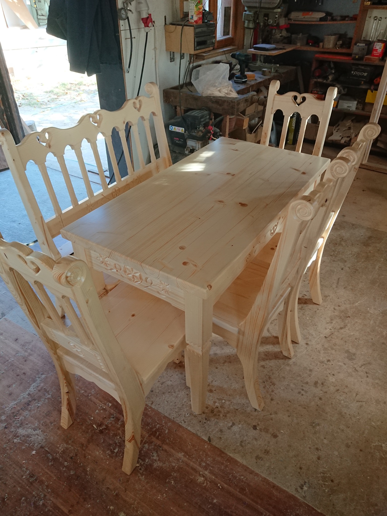 Surowy, drewniany stół z czterema krzesłami i ławką, z dekoracyjnymi wycięciami i zdobieniami w warsztacie stolarskim.