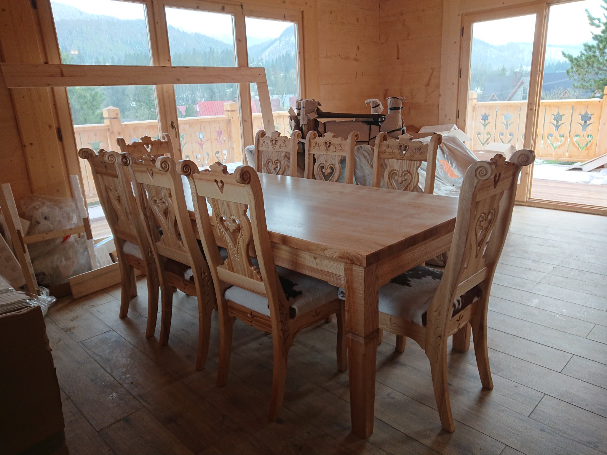 Drewniany stół z ośmioma krzesłami w surowym drewnianym wnętrzu z widokiem na góry i drewniany balkon.