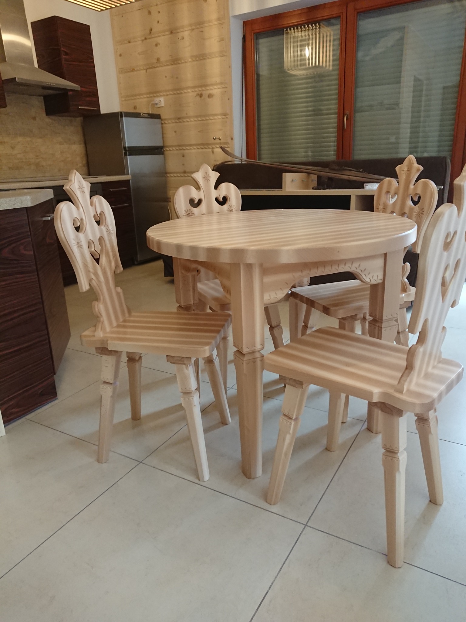 Drewniany stół z czterema krzesłami o zdobionych oparciach w stylu góralskim, widoczne w kuchni z drewnianą boazerią.