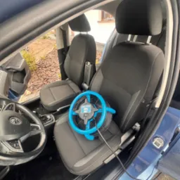 Wnętrze niebieskiego samochodu z czarną tapicerką, na siedzeniu pasażera leży niebieski wentylator marki Dri-Pod podłączony kablem do gniazdka, prawdopodobnie w celu osuszenia po czyszczeniu.