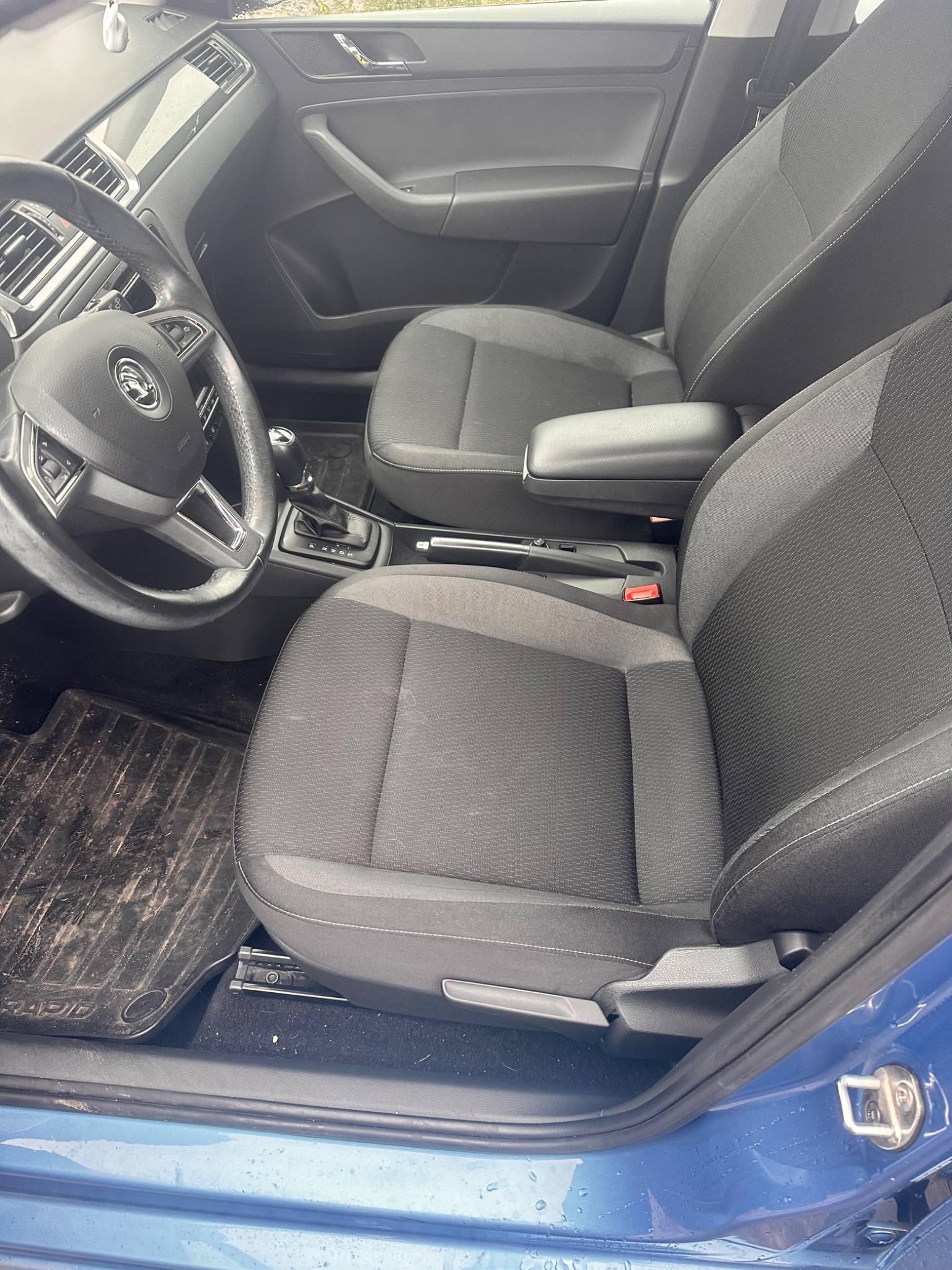 Wnętrze samochodu w Pułtusku, z widocznymi czarnymi fotelami z tapicerką, kierownicą z logo Skoda i zabrudzonym dywanikiem podłogowym.