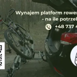 Platforma rowerowa zamontowana na haku holowniczym samochodu, z rowerem, na tle lasu, z widocznym kodem QR i numerem telefonu.