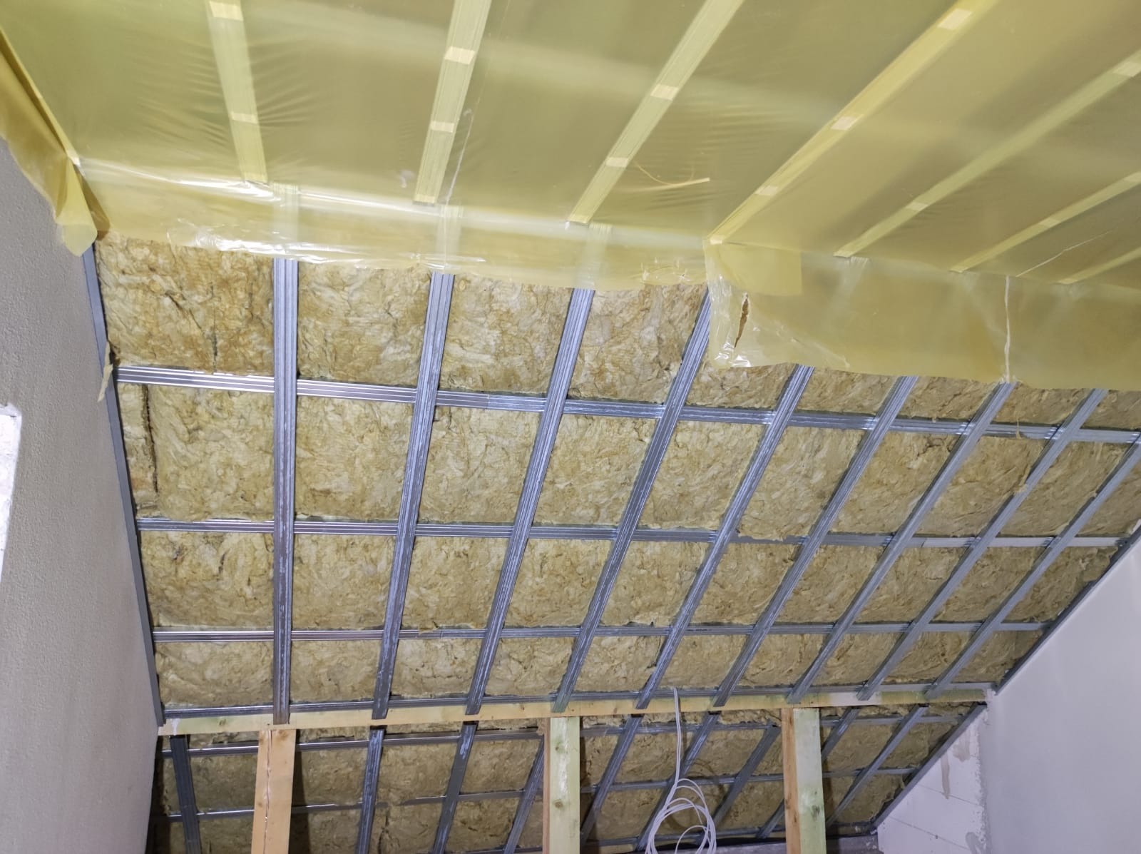 Montaż izolacji z wełny mineralnej w metalowym stelażu na poddaszu w Zielonej Górze, widoczna folia paroizolacyjna i fragment instalacji elektrycznej.