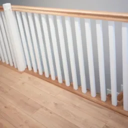Nowoczesna balustrada schodowa z białymi pionowymi szczeblami i drewnianym poręczą, zamontowana na drewnianej podłodze.