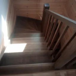 Widok z góry na drewniane schody z balustradą w domu w Wieczfni Kościelnej, z widoczną strukturą drewna i mocnym światłem wpadającym z boku.