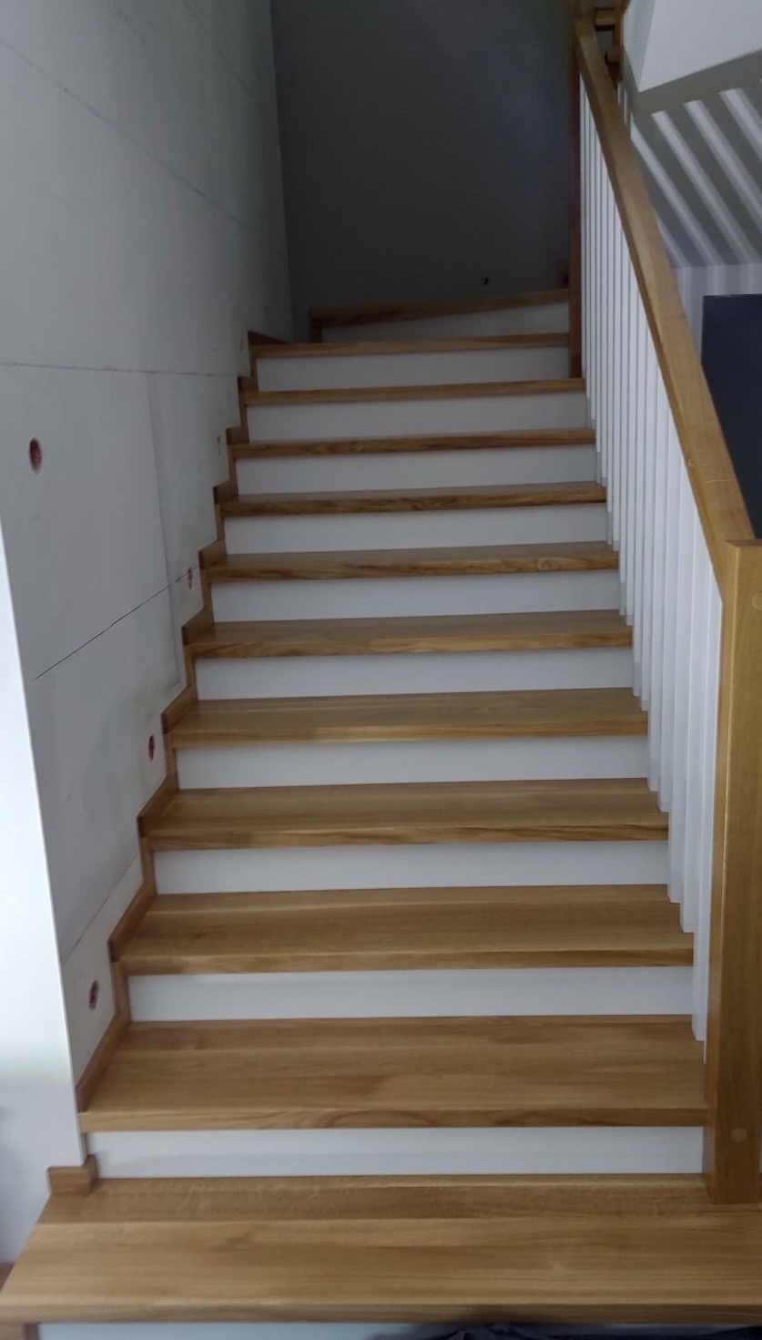 Jasne drewniane schody z białymi podstopnicami i drewnianą balustradą, widok z dołu na górę, minimalistyczny design.