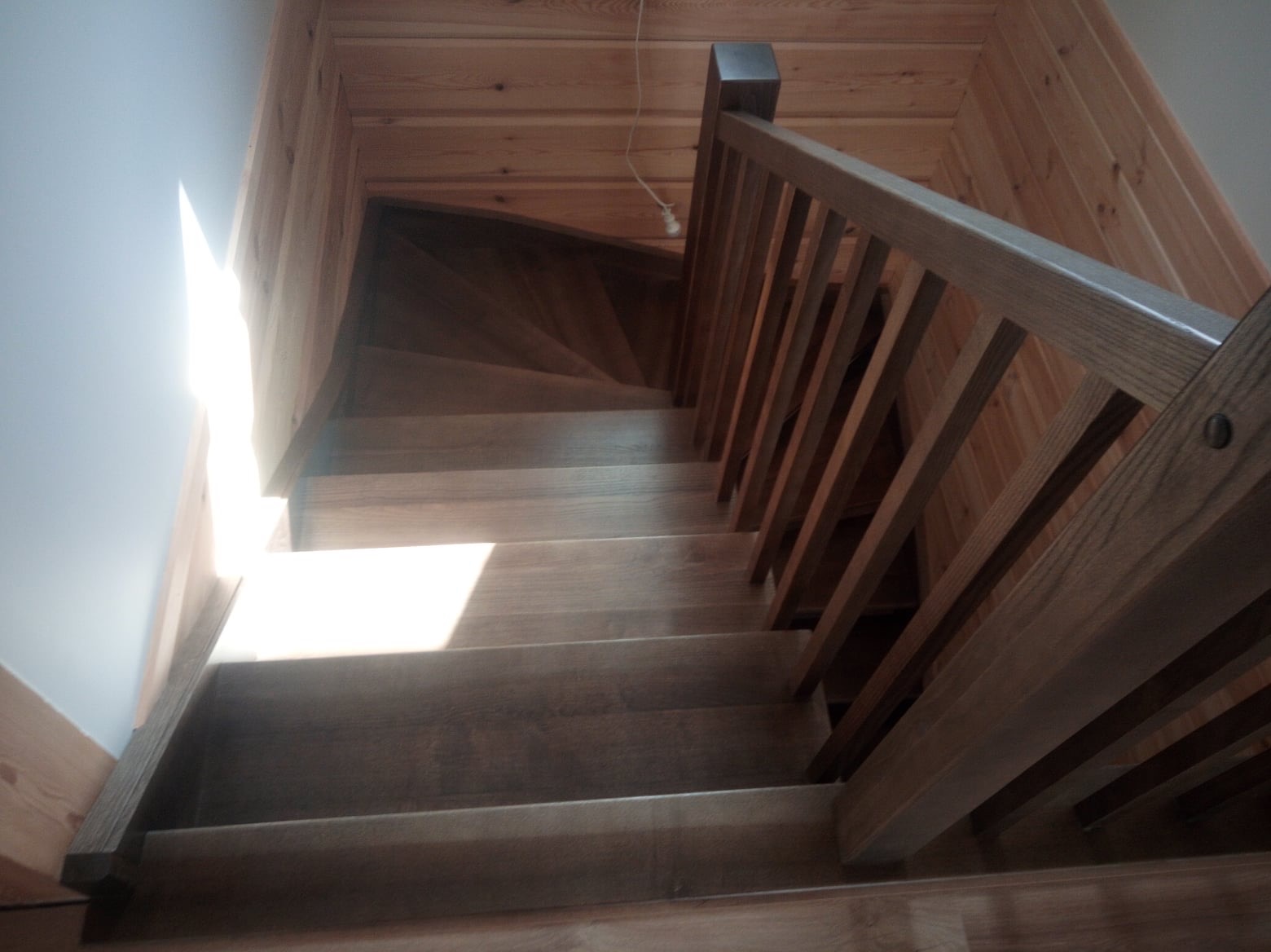 Widok z góry na drewniane schody z balustradą w domu w Wieczfni Kościelnej, z widoczną strukturą drewna i mocnym światłem wpadającym z boku.