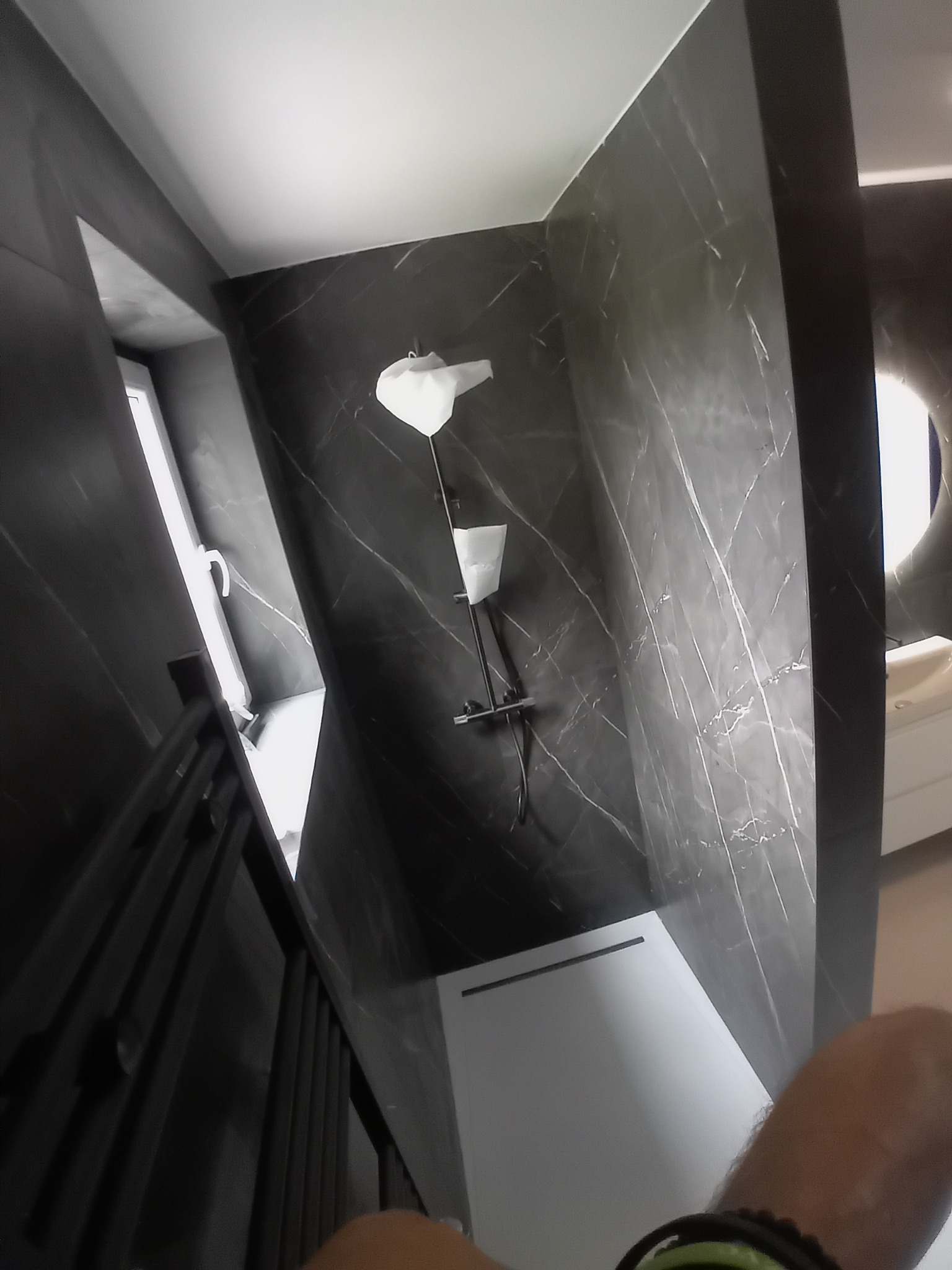 Nowoczesna kabina prysznicowa z deszczownicą i panelami imitującymi marmur. Widok z dołu, podkreślający wysokość i przestronność kabiny.