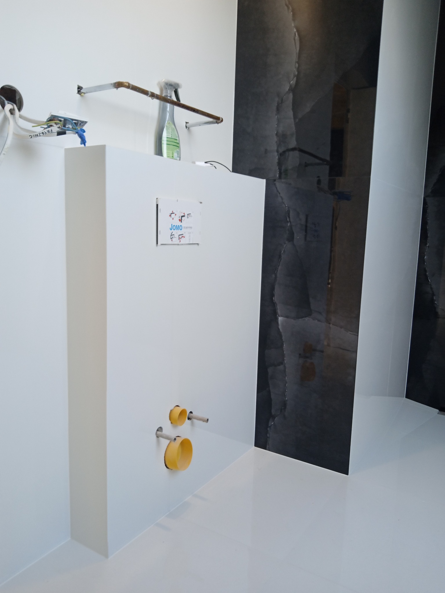 Montaż podtynkowego systemu WC z widocznymi rurami doprowadzającymi wodę i czarnymi płytkami imitującymi kamień na ścianie w nowoczesnej łazience.