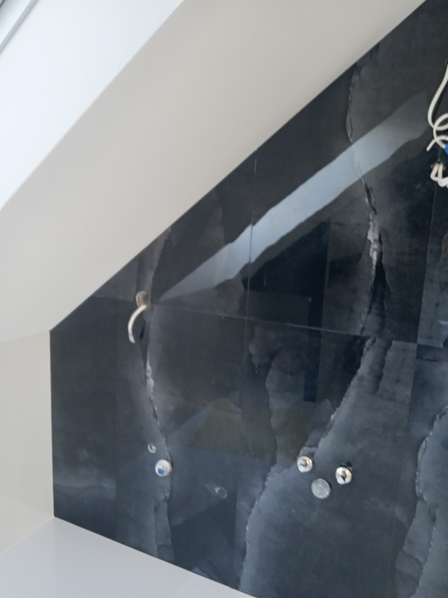 Fragment ściany w łazience wyłożonej czarnymi płytkami imitującymi kamień, widoczne otwory na armaturę i wystające przewody elektryczne, biały sufit pod skosem.