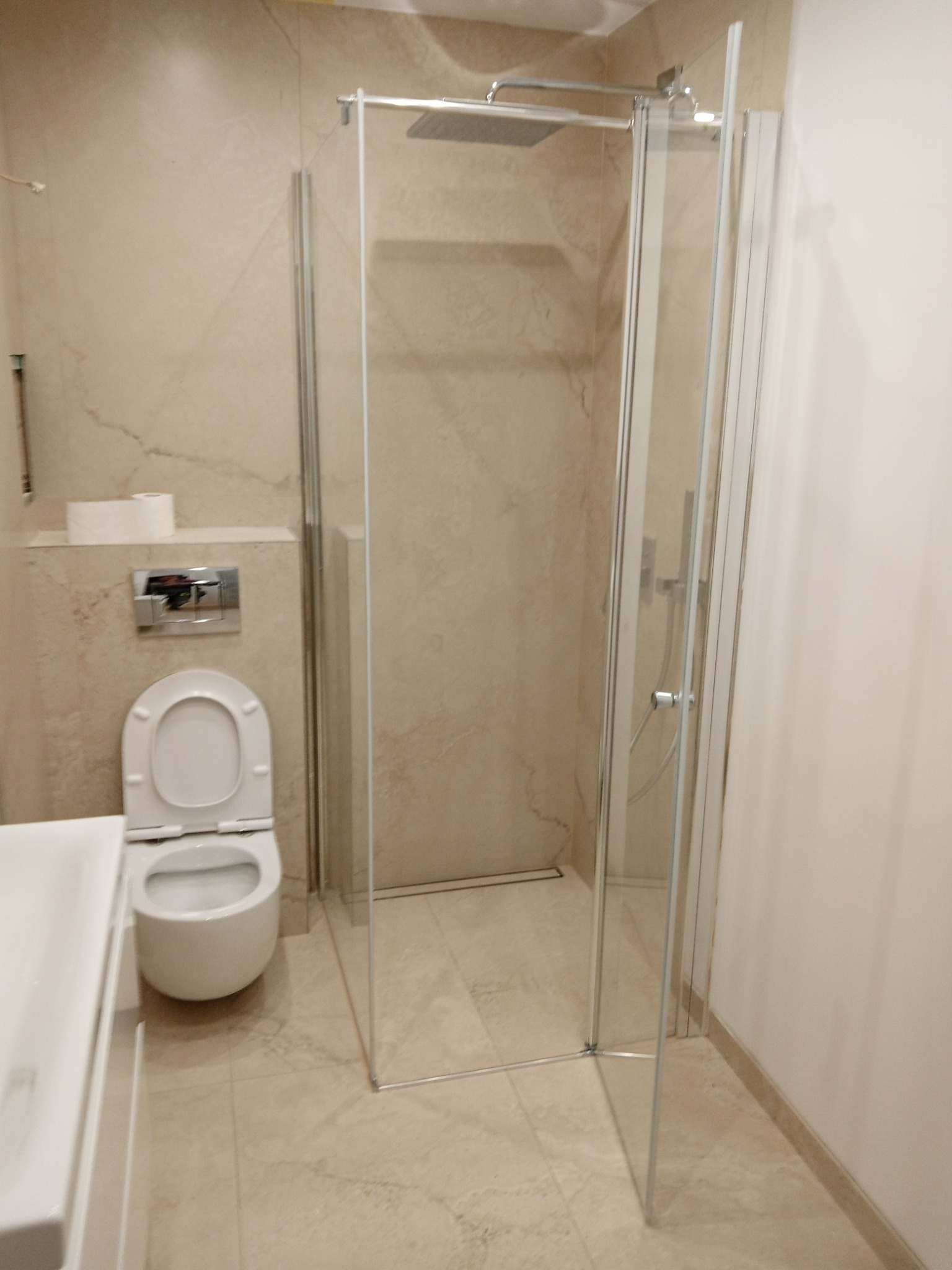 Wykończona łazienka w beżowych tonacjach z kabiną prysznicową typu walk-in, podwieszaną toaletą i umywalką, płytki imitujące marmur na ścianach i podłodze.