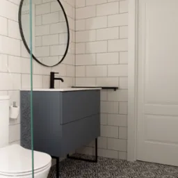 Nowoczesna łazienka z szarą szafką pod umywalką, okrągłym lustrem w czarnej ramie, białą armaturą, białą cegłą na ścianach i wzorzystą czarno-białą podłogą.