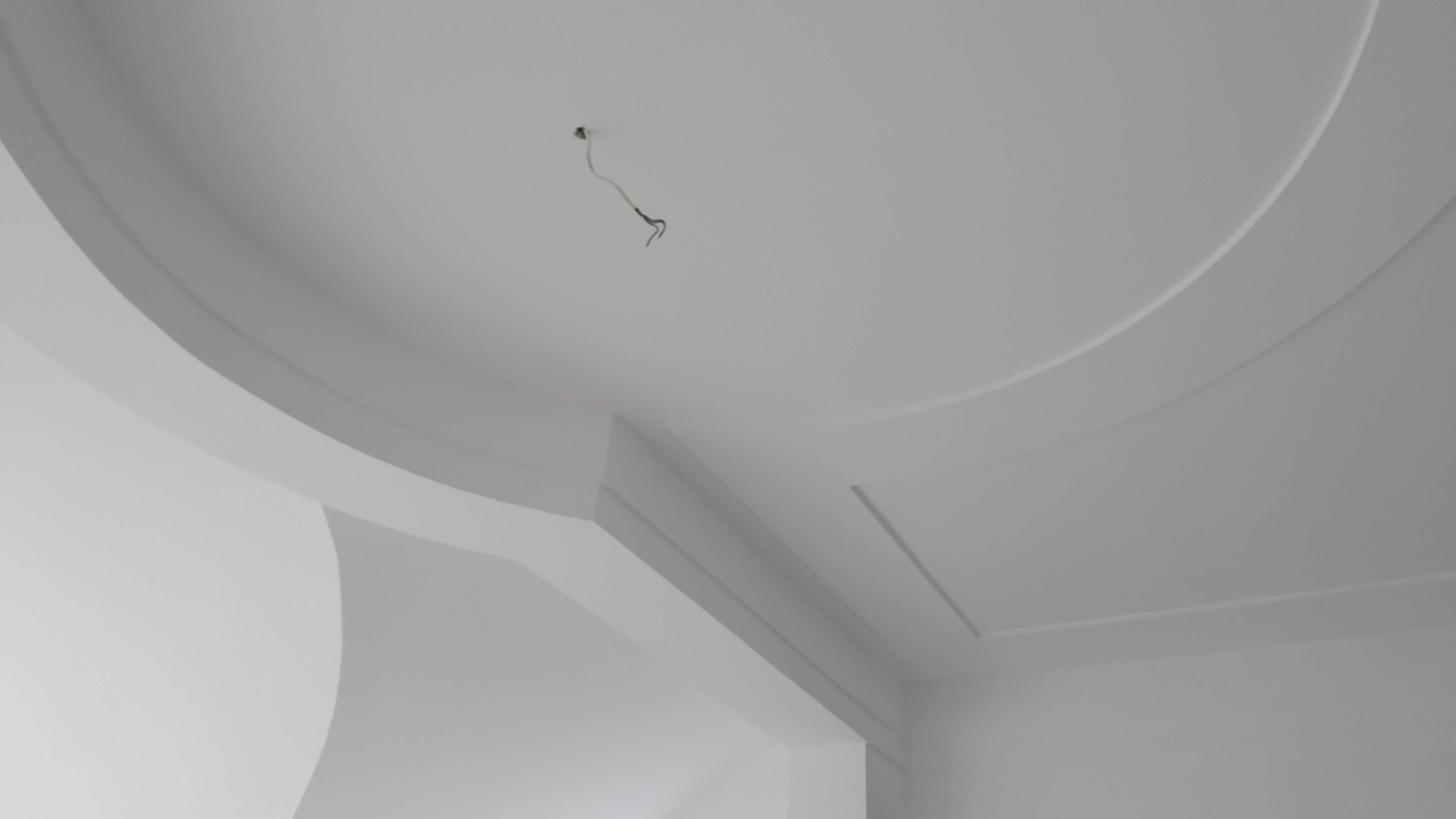 Biały sufit z dekoracyjnymi elementami gipsowymi: okrągłe wgłębienie i listwy, widoczne kable oświetleniowe.