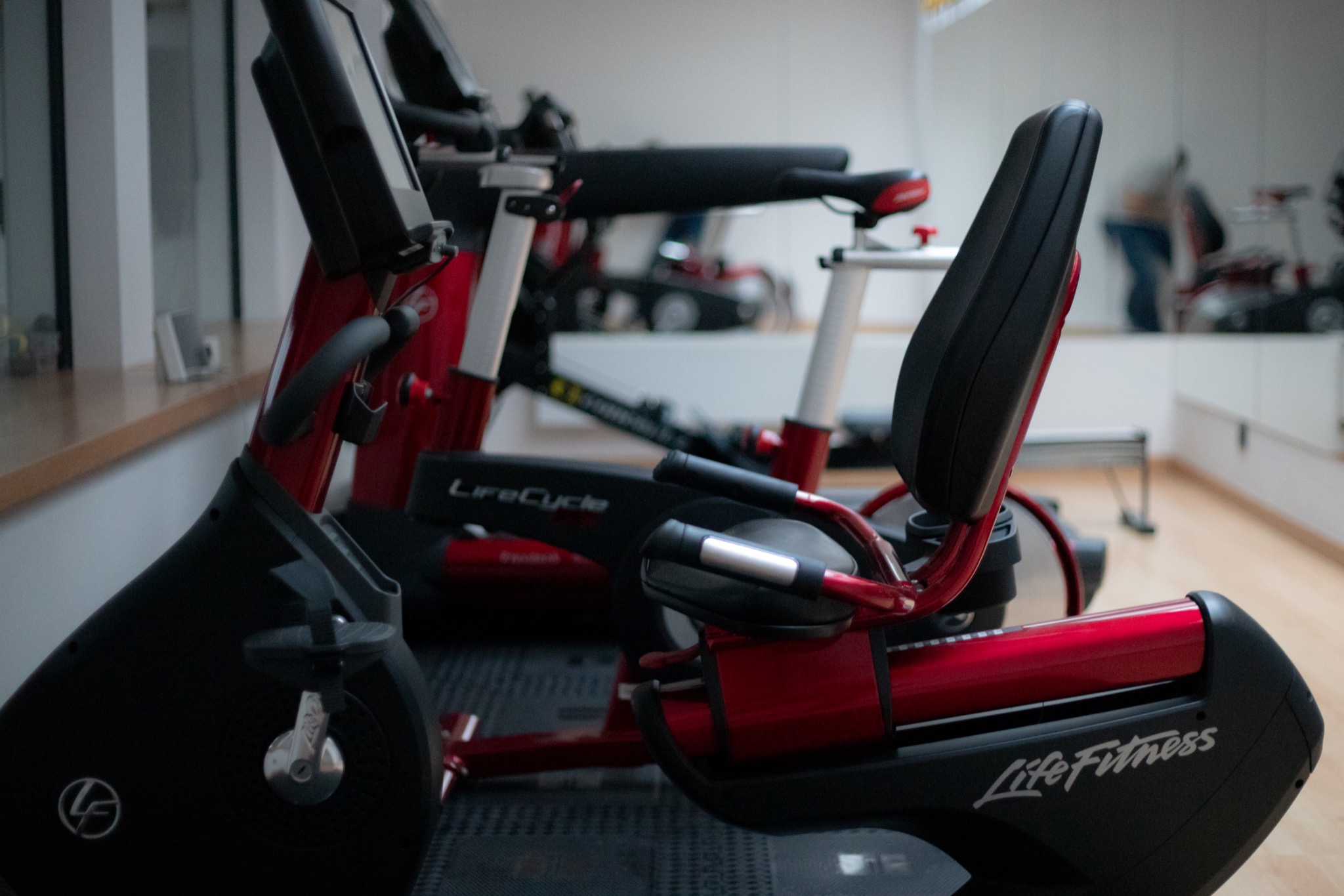 Rząd stacjonarnych rowerów treningowych Life Fitness w jasnym pomieszczeniu z lustrem, widoczne detale konstrukcyjne i logo producenta.