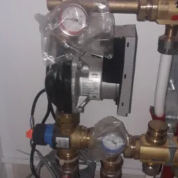 Węzeł cieplny z pompą obiegową Wilo Yonos Para, zaworami odcinającymi z czerwonymi rączkami i manometrami w foliowych osłonach, widoczne rury miedziane i plastikowe.