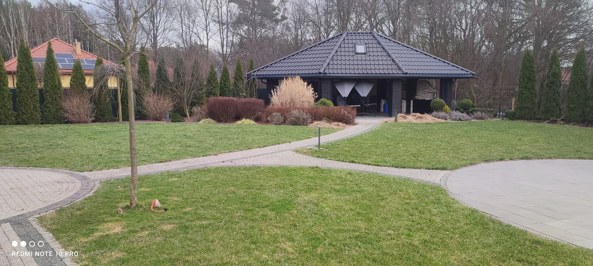 Zadbany ogród w Stalowej Woli z równo przystrzyżonym trawnikiem, ścieżką z kostki brukowej prowadzącą do altany z grillem i starannie dobraną roślinnością.