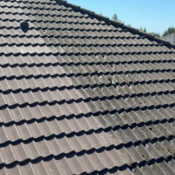 Loba FrogForce - Ciemnobrązowa dachówka ceramiczna pokryta mchem i zabrudzeniami, widok z góry na fragment dachu z kominem wentylacyjnym, błękitne niebo w tle.