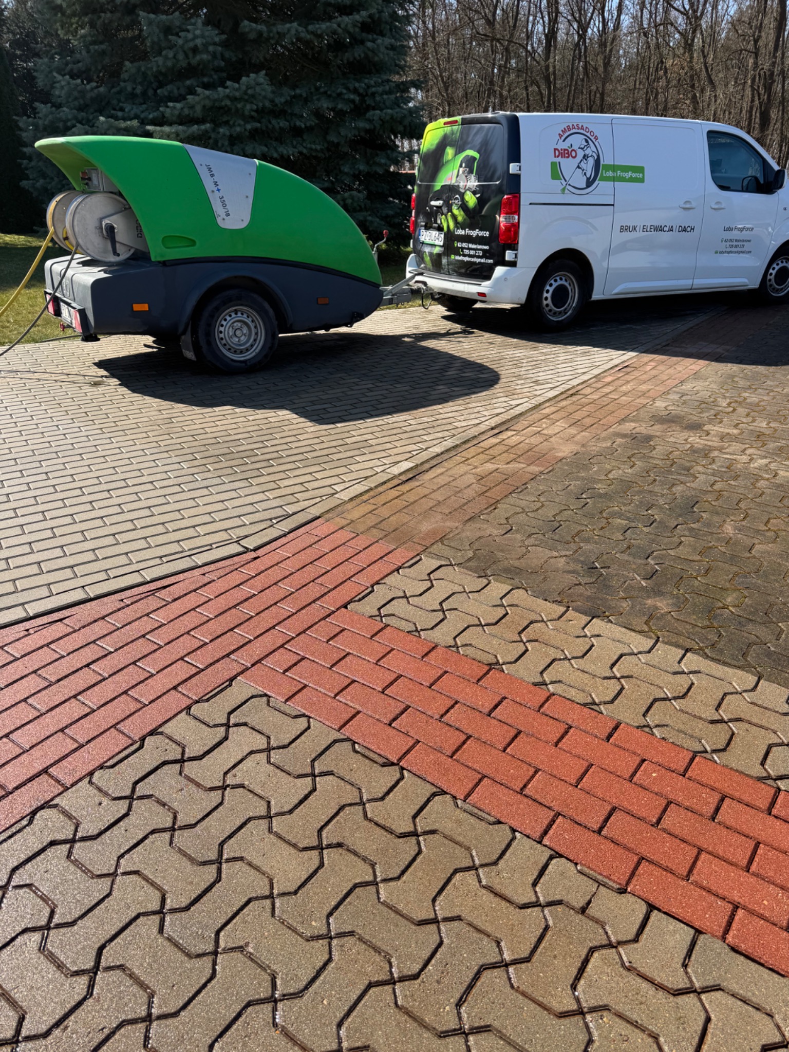 Częściowo wyczyszczona kostka brukowa z widoczną różnicą w kolorze, przyczepa z myjką ciśnieniową i samochód dostawczy firmy sprzątającej w tle.