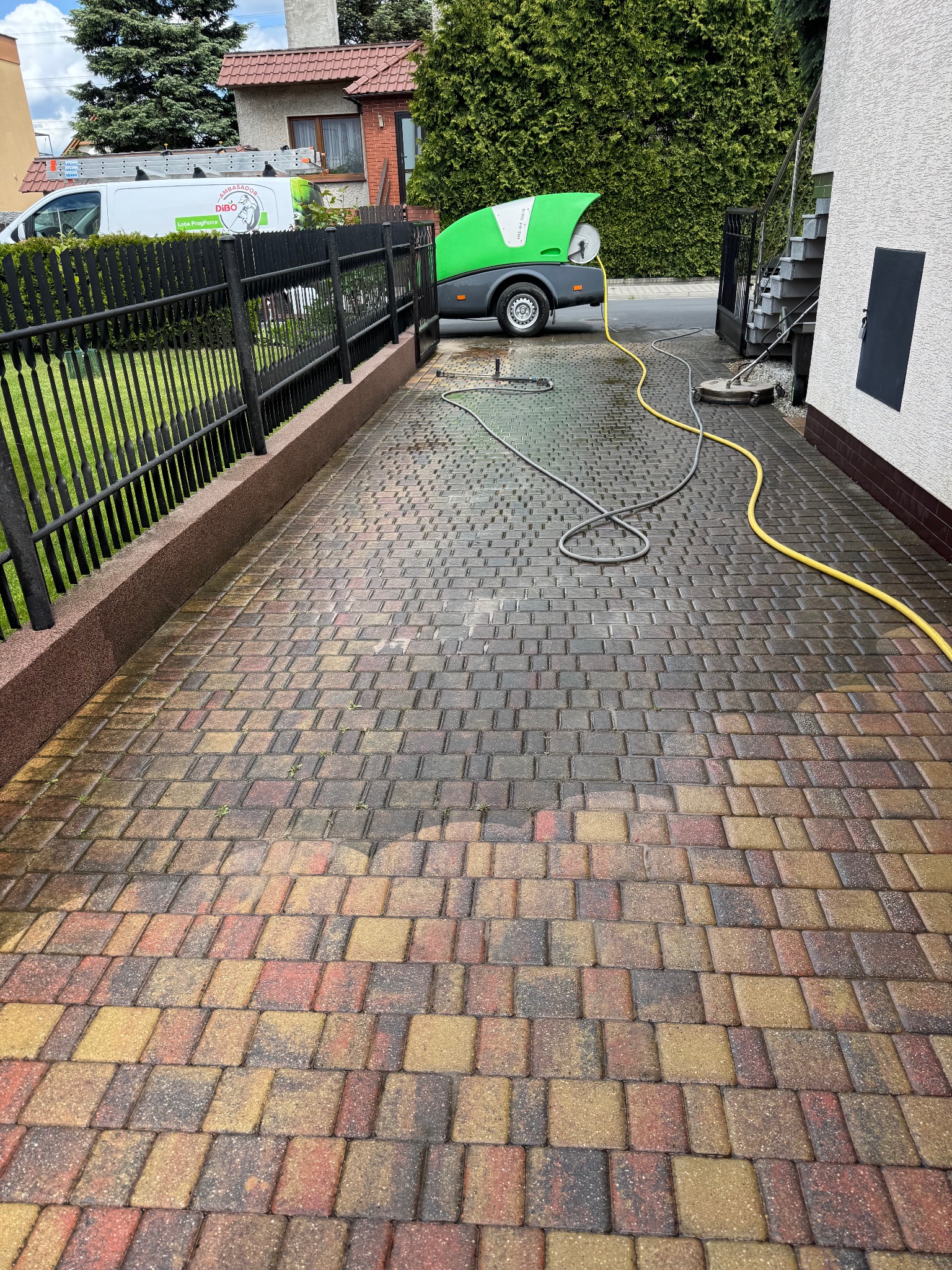 Czyszczenie kostki brukowej z użyciem specjalistycznego sprzętu. Widoczny efekt mycia, różnica w kolorze kostki. Żółty wąż i szara lanca na mokrej powierzchni.