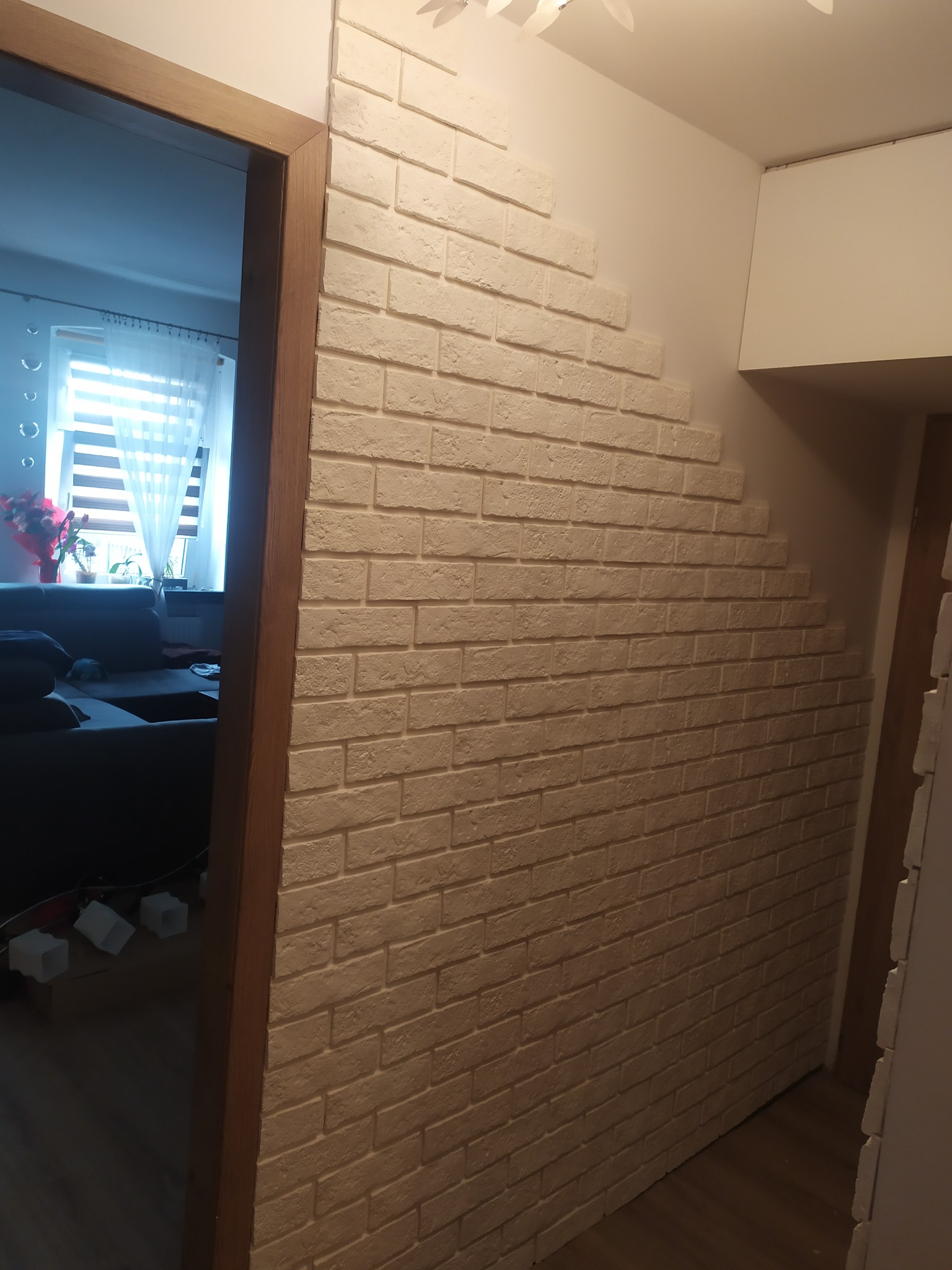 Dekoracyjna ściana z białej cegły w przedpokoju, widok z perspektywy drzwi, z fragmentem salonu w tle.