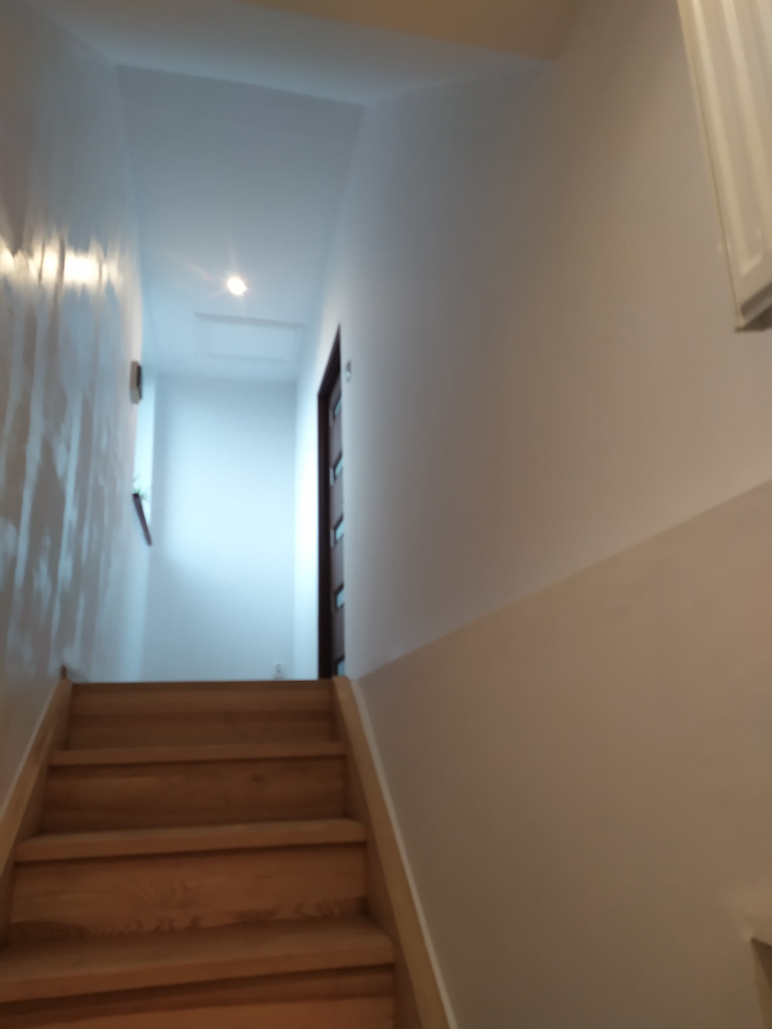 Schody drewniane prowadzące na poddasze w Pszowie, z widocznymi świeżo pomalowanymi ścianami w jasnym odcieniu.