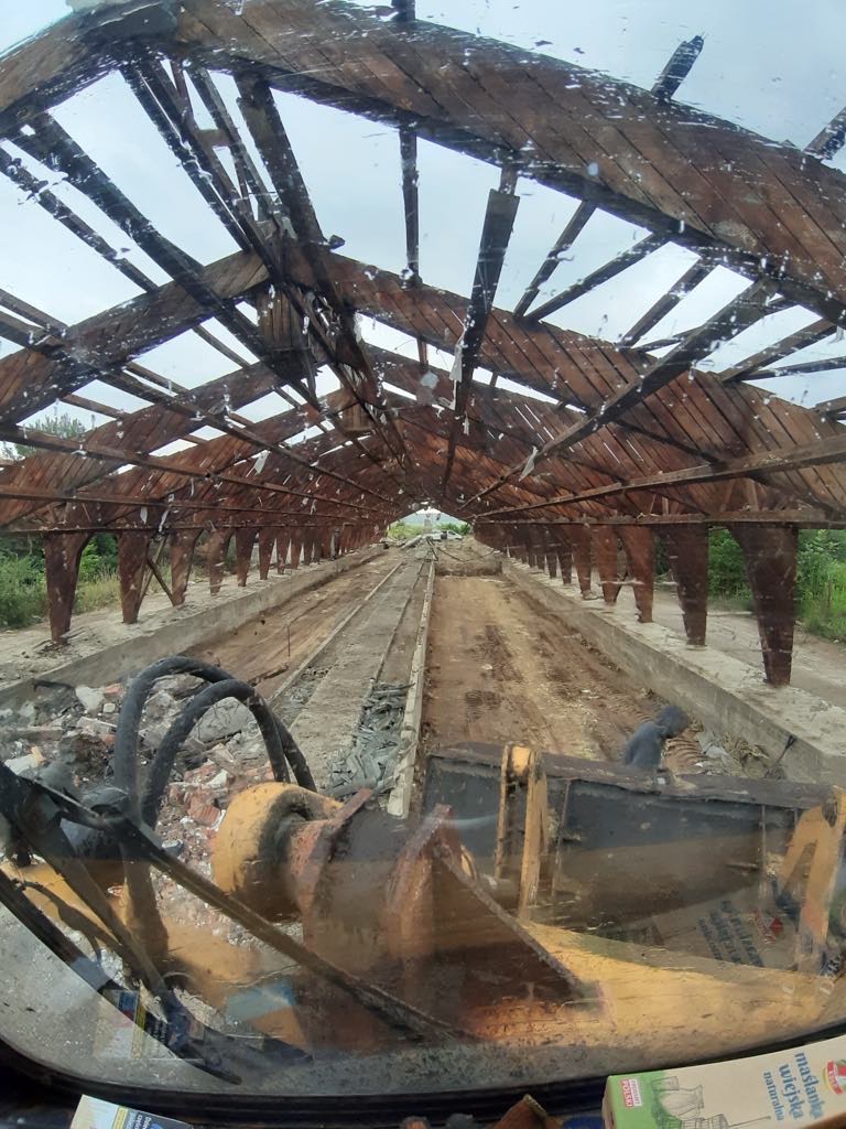 Wnętrze rozebranego budynku z drewnianą konstrukcją dachu, widok z kabiny maszyny budowlanej na gruz i pozostałości po rozbiórce.