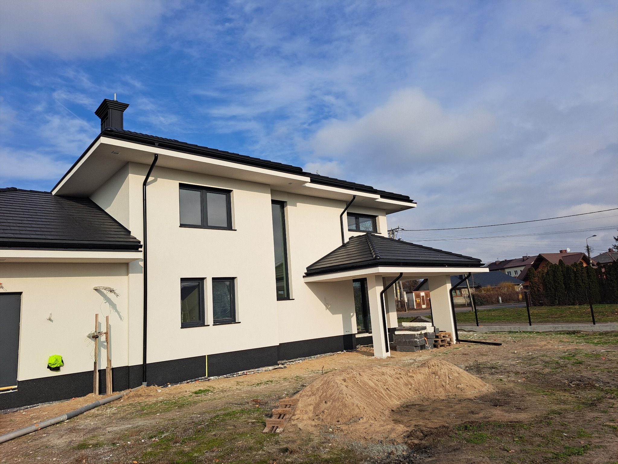 Nowoczesny dom z białą elewacją i czarną stolarką okienną, widoczny z zewnątrz w słoneczny dzień. Uwagę zwraca kontrast kolorów i minimalistyczny design.