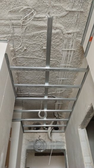 Montaż metalowej konstrukcji sufitu podwieszanego z widocznymi przewodami elektrycznymi w surowym stanie.