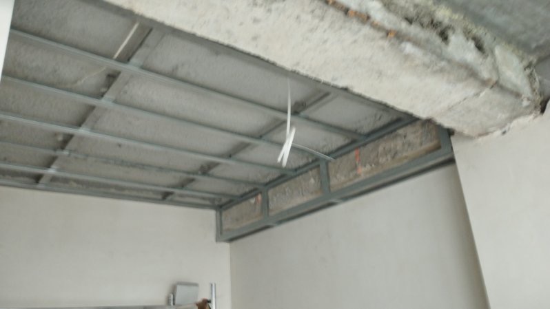 Metalowa konstrukcja sufitu podwieszanego w trakcie montażu, widoczne przewody elektryczne, surowy betonowy strop powyżej.