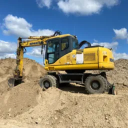 Żółta koparka kołowa Komatsu stoi na usypanej pryzmie piasku pod błękitnym niebem z białymi chmurami.