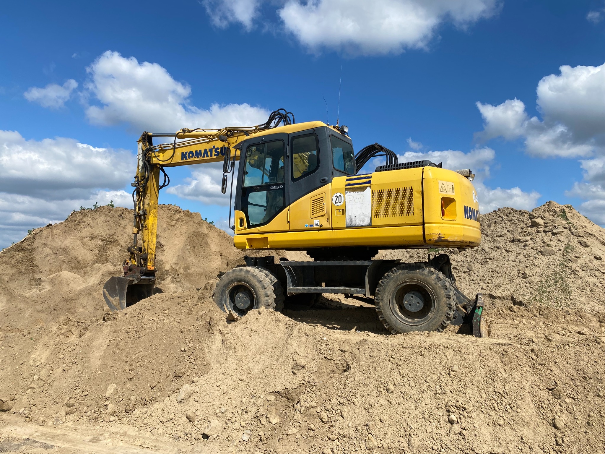 Żółta koparka kołowa Komatsu stoi na usypanej pryzmie piasku pod błękitnym niebem z białymi chmurami.