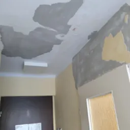 Przygotowanie sufitu i ściany do dalszych prac wykończeniowych, widoczne fragmenty starej farby i nałożona warstwa szpachli, sufit w trakcie wyrównywania.