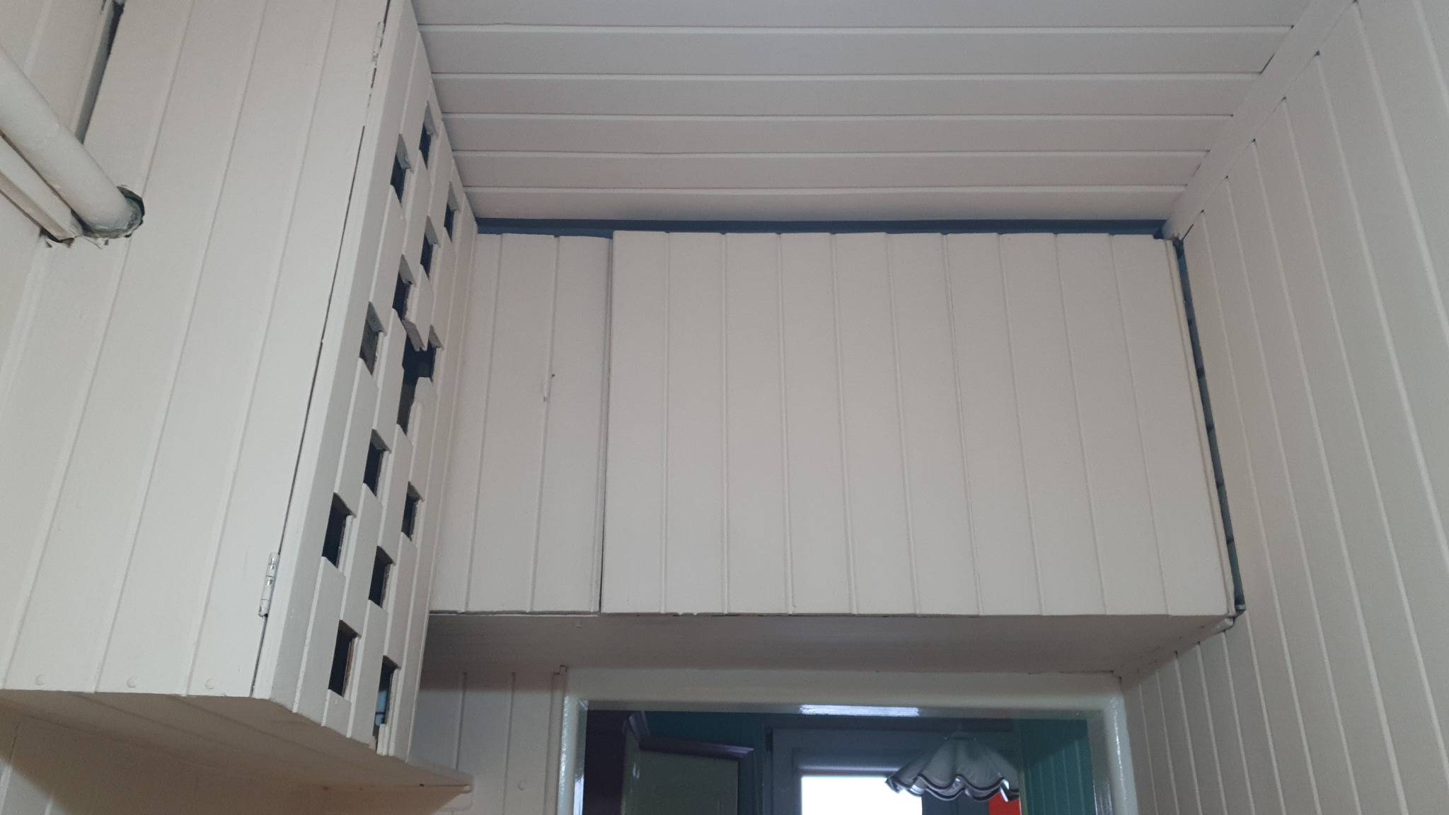 Białe panele boazeryjne na ścianach i suficie, widoczne nadproże drzwi, oświetlenie sufitowe.