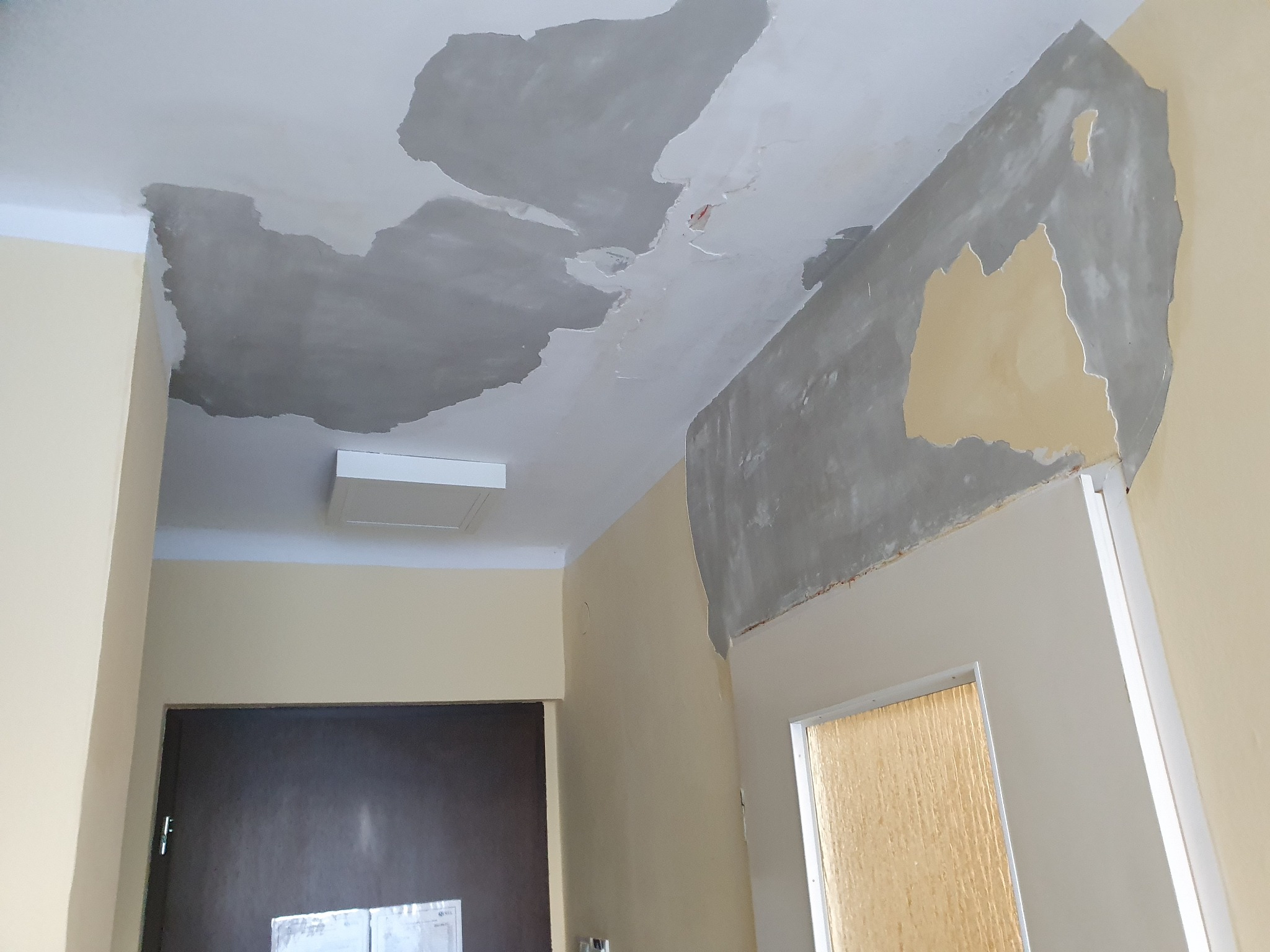 Przygotowanie sufitu i ściany do dalszych prac wykończeniowych, widoczne fragmenty starej farby i nałożona warstwa szpachli, sufit w trakcie wyrównywania.