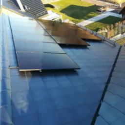 Czarny dach pokryty panelami słonecznymi, widok z góry, w tle zadbany ogród i zabudowania.