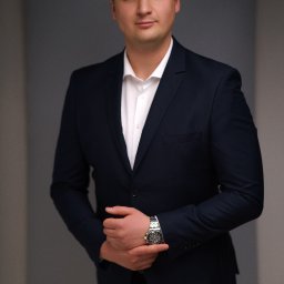 Wiesław Kozłowski Fotografia - Mężczyzna w granatowym garniturze i białej koszuli, z zegarkiem na ręce, pozuje na neutralnym tle.