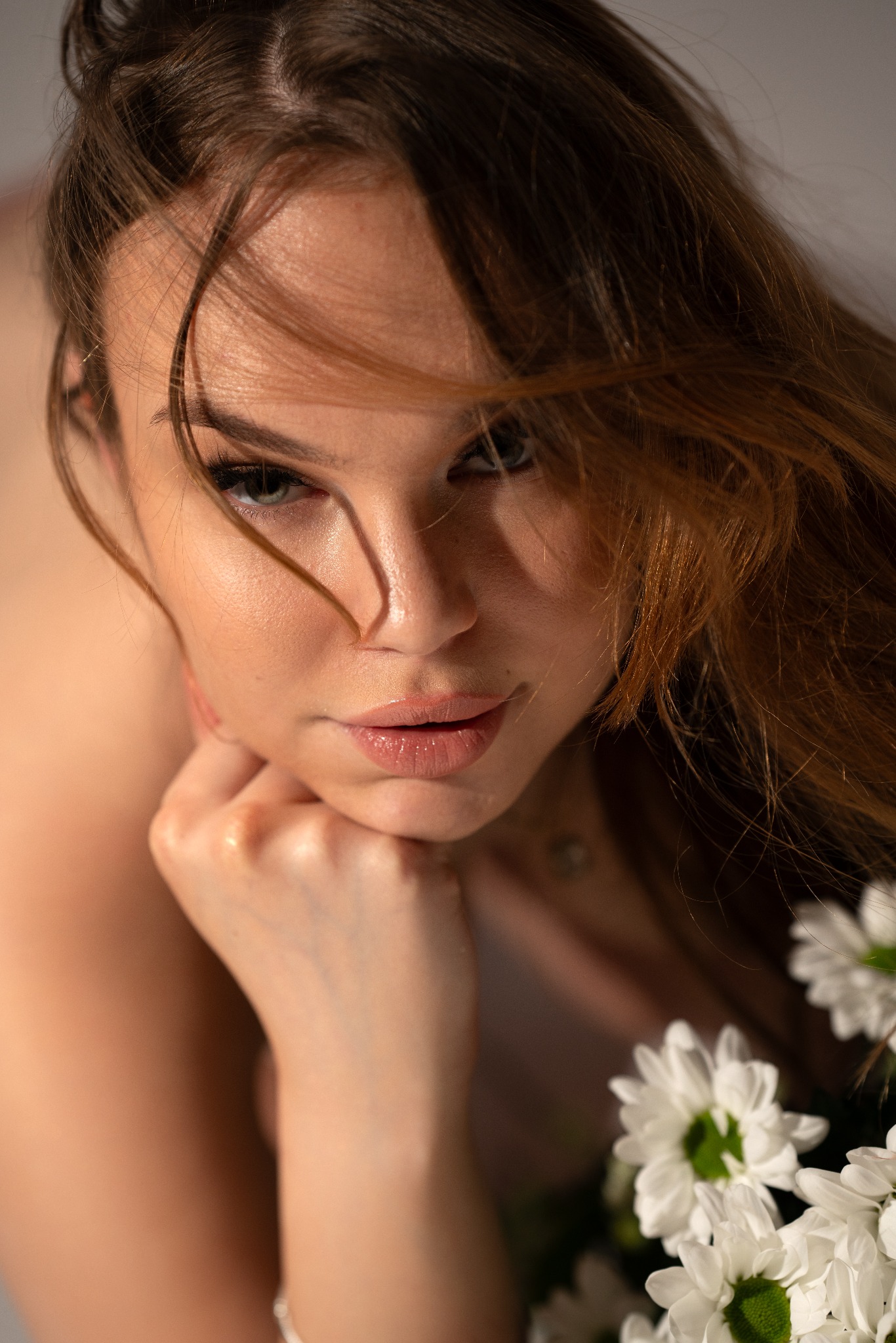 Portret kobiety z rozpuszczonymi włosami, opierającej podbródek na dłoni, z bukietem białych kwiatów w dolnym rogu.