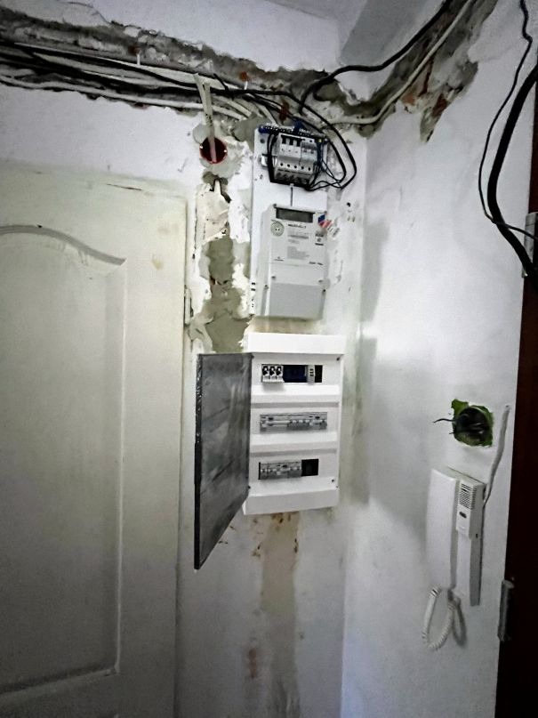 Rozdzielnia elektryczna po modyfikacji, widoczny licznik energii, zabezpieczenia oraz otwarte drzwiczki rozdzielni na tle ściany w trakcie remontu.