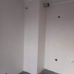 Olexbud Grzegorz Oleksy - Wnętrze po świeżym pomalowaniu ścian na jasny odcień, widoczne gniazdka elektryczne i rura wentylacyjna przy suficie, szara podłoga z wzorem marmuru.