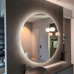 MICHBUD MICHAŁ KOWALSKI - Nowoczesna łazienka z okrągłym lustrem podświetlanym LED, szara umywalka nablatowa i minimalistyczna armatura, wiszące lampy kuliste, widoczne elementy wykończeniowe na podłodze.