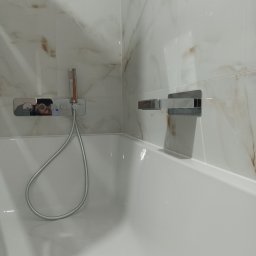 MICHBUD MICHAŁ KOWALSKI - Biała wanna z zamontowaną baterią i prysznicem na tle marmurowych płytek z brązowymi żyłkami.