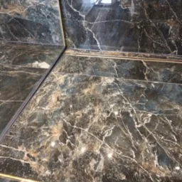 Ciemne, marmurowe płytki na ścianie z delikatnymi złotymi listwami dekoracyjnymi, widoczne odbicie światła na powierzchni płytek.