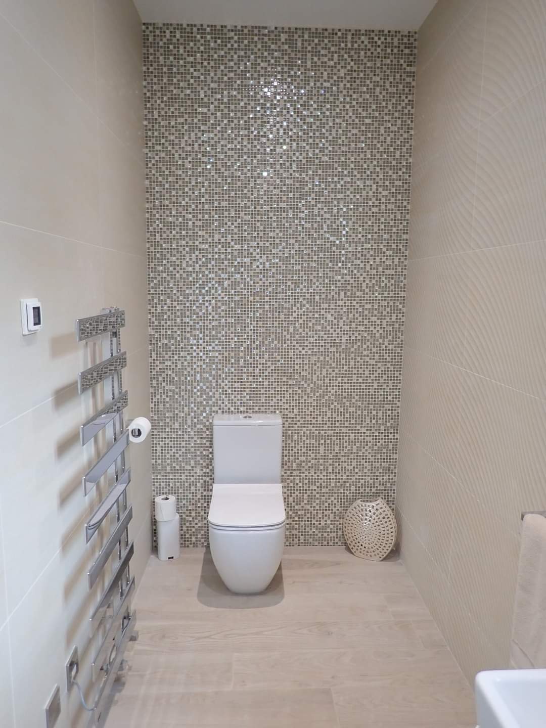 Nowoczesna łazienka z mozaiką na ścianie, wisząca toaleta, grzejnik drabinkowy i podłoga z paneli imitujących drewno.