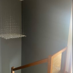 Jakub Ziemiański - Ściana pomalowana na szaro w korytarzu ze szklaną balustradą i nowoczesnym żyrandolem z kryształków.